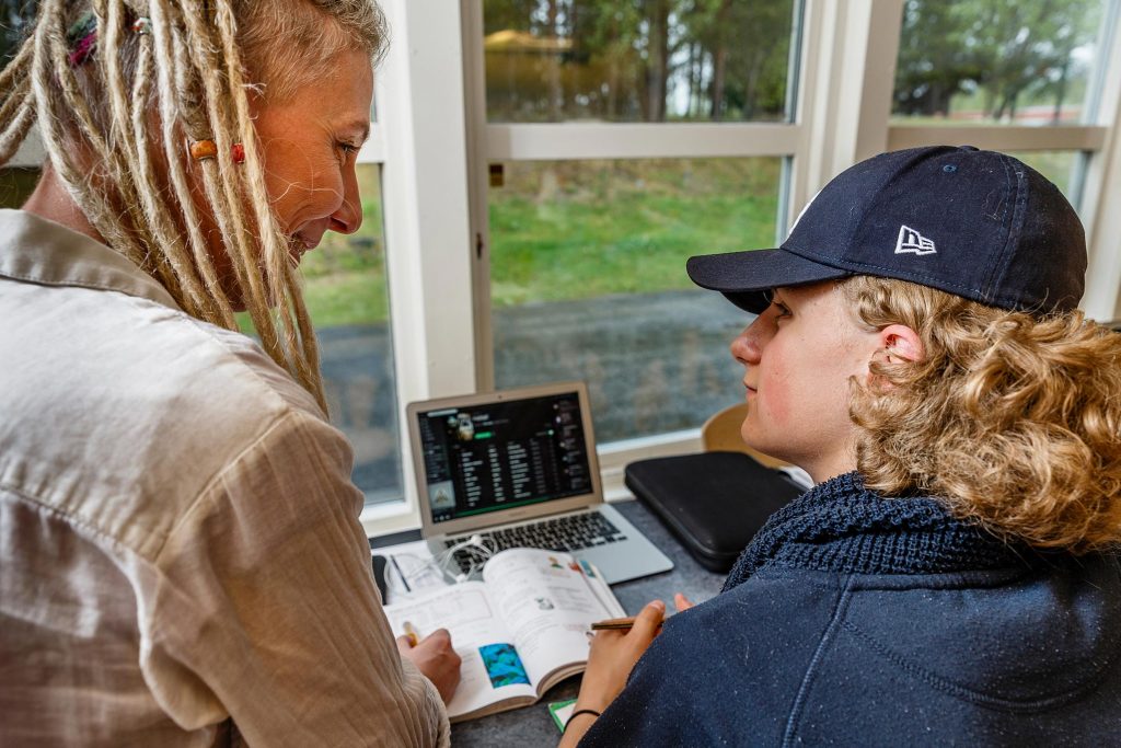 Tonårig kille interagerar med kvinna. På bordet framför dem finns en bärbar dator och en uppslagen bok.